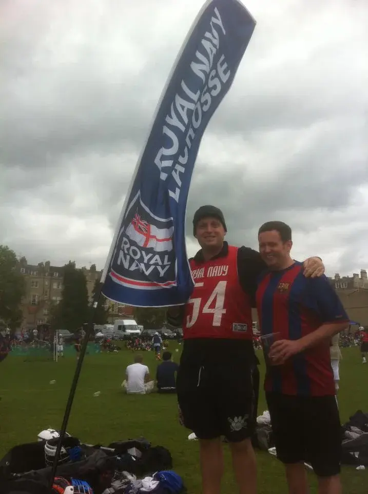 Two men standing on a field, one holding a Royal Navy flag.