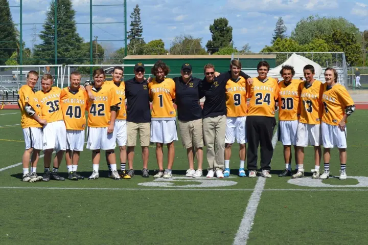 Youth lacrosse team and coaches gathered on a field.